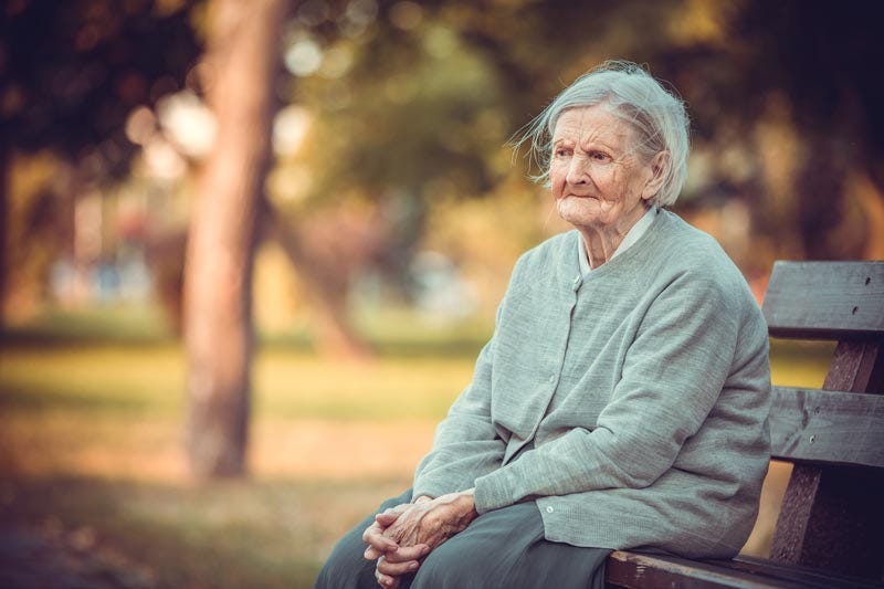 Isolated elder woman sitting alone on park bench