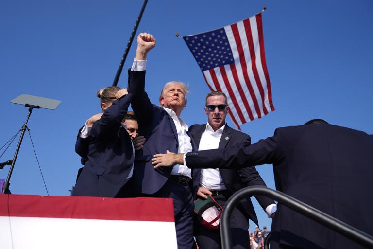 Republican presidential candidate former President Donald Trump gestures as he is surrounded by U.S. Secret Service agents as he leaves the stage at a campaign rally, Saturday, July 13, 2024, in Butler, Pennsylvania.