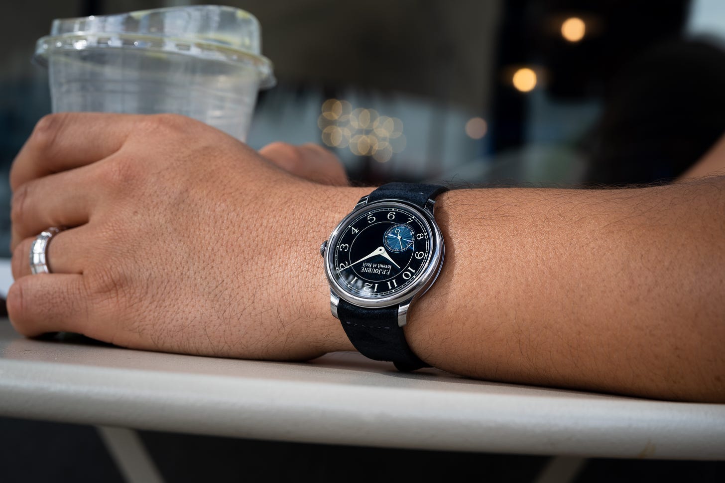 arm resting on table, holding an empty cup, wearing a watch