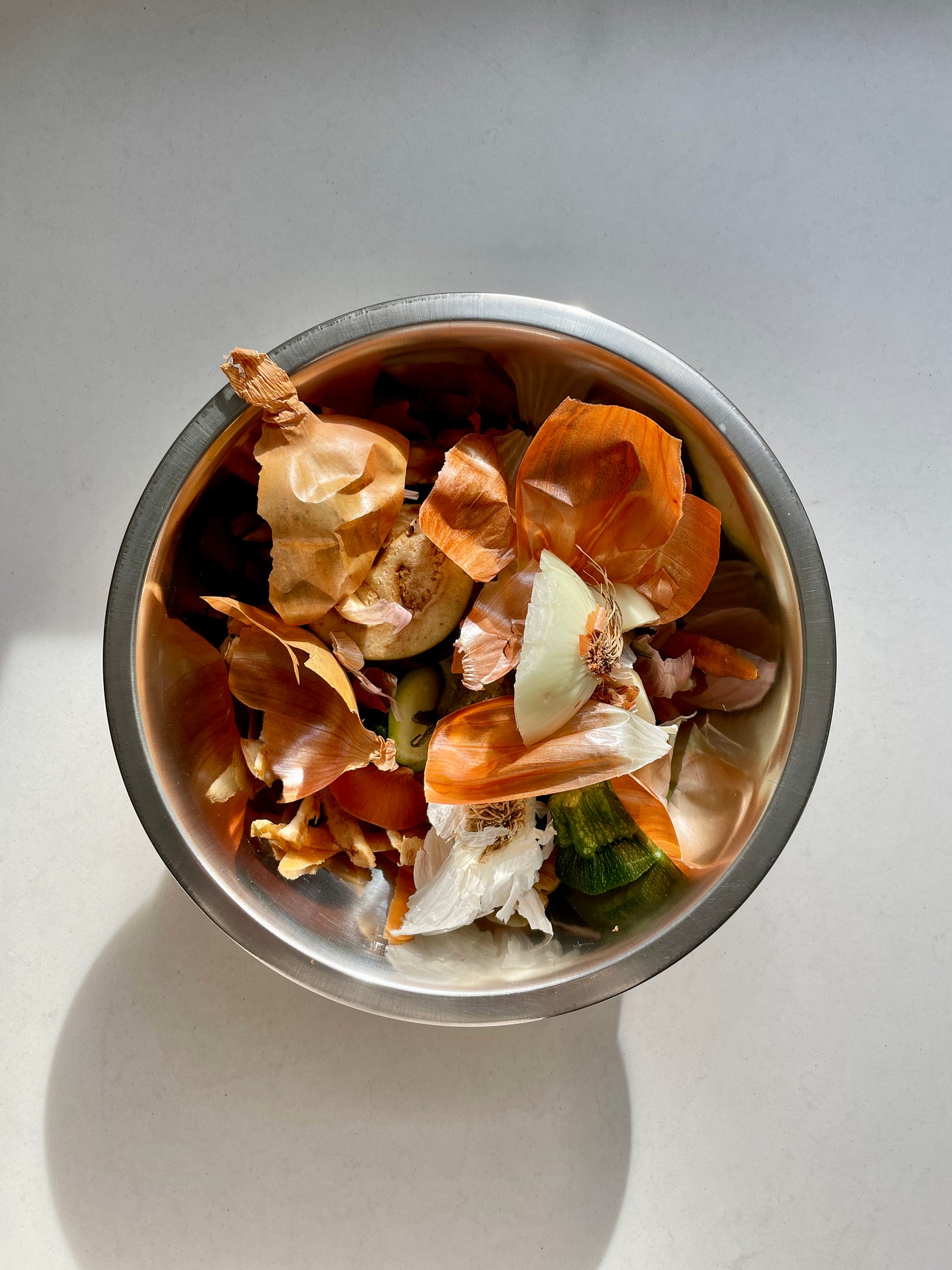 A top-down view of a silver bowl full of vegetable scraps and peelings.