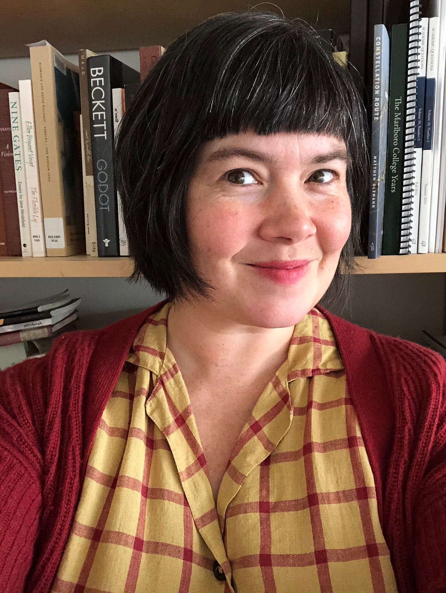 Bronwen Tate author photo: a woman with bangs and a bob smiles in front of a bookshelf