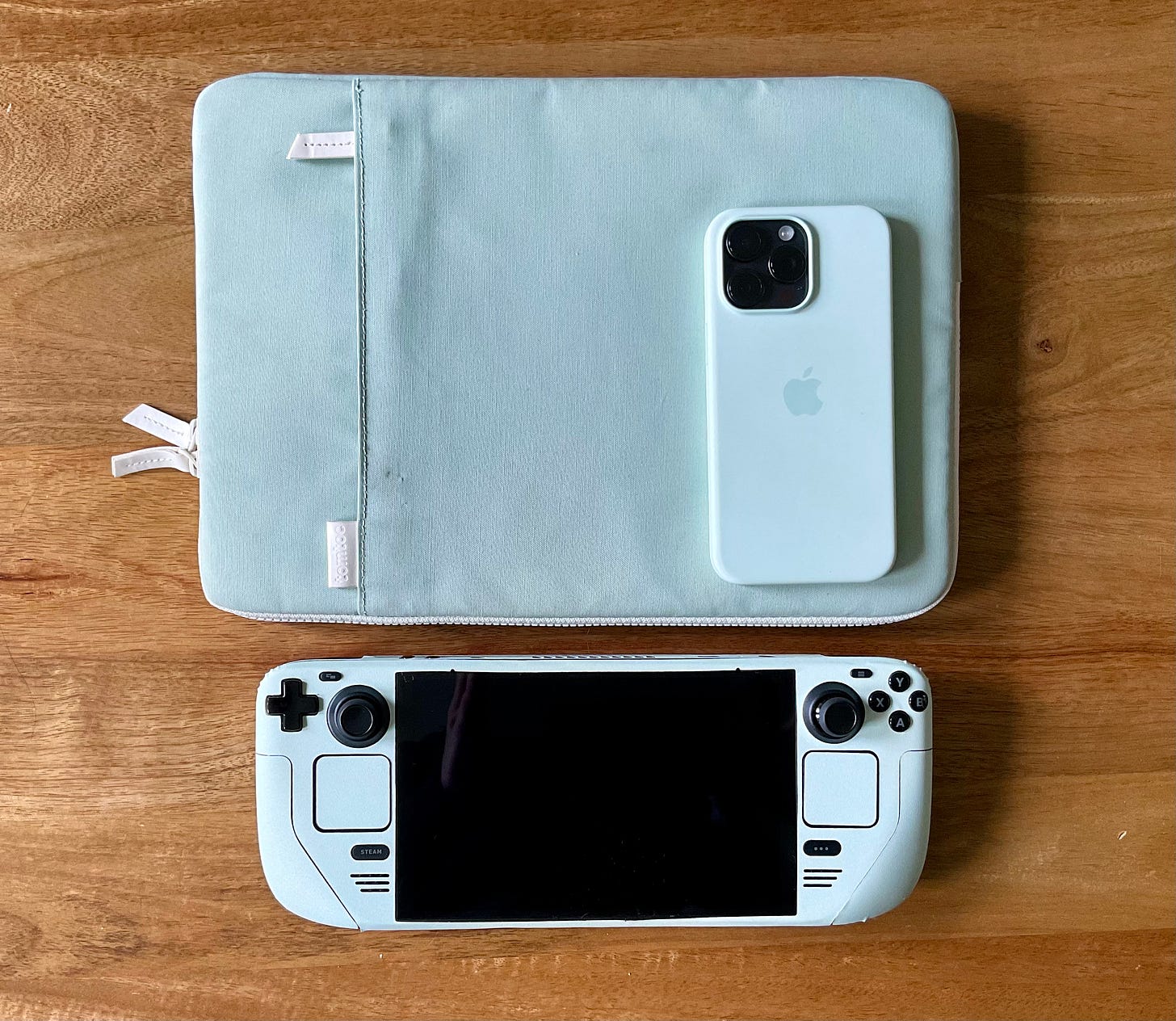 A laptop case, phone and steam deck all in the same colour of light mint green