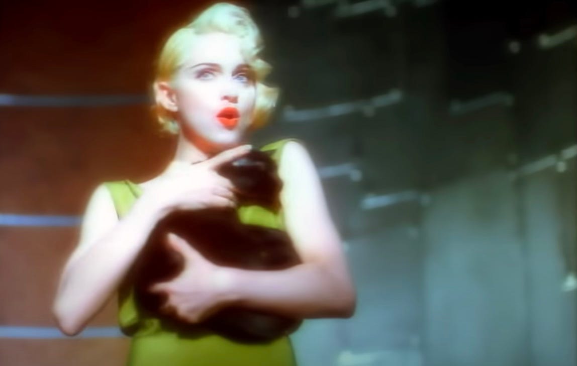 Madonna wears a green dress and holds a cat in her arms