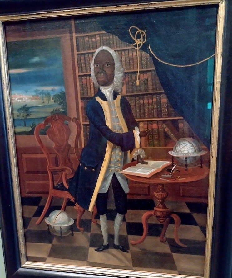 Black man in 18th century dress, including wig, standing before bookcase, with scene of island and palm trees seen through window behind him
