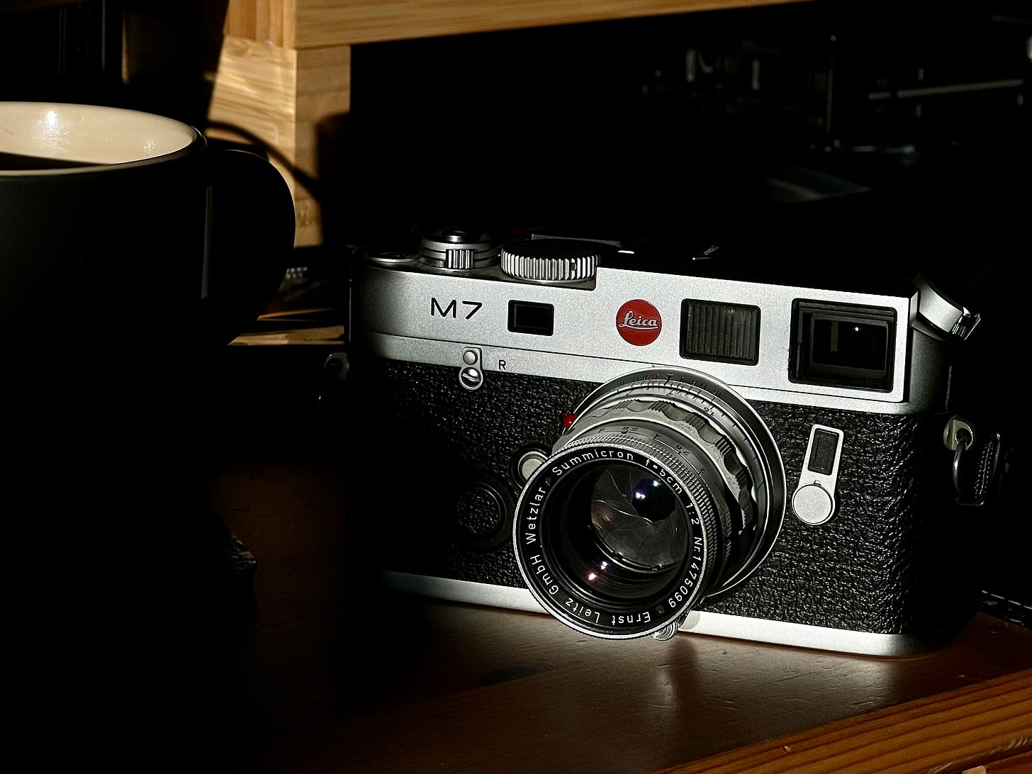 A Leica M7 film camera with a 50mm lens sat on a desk next to a cup of tea.