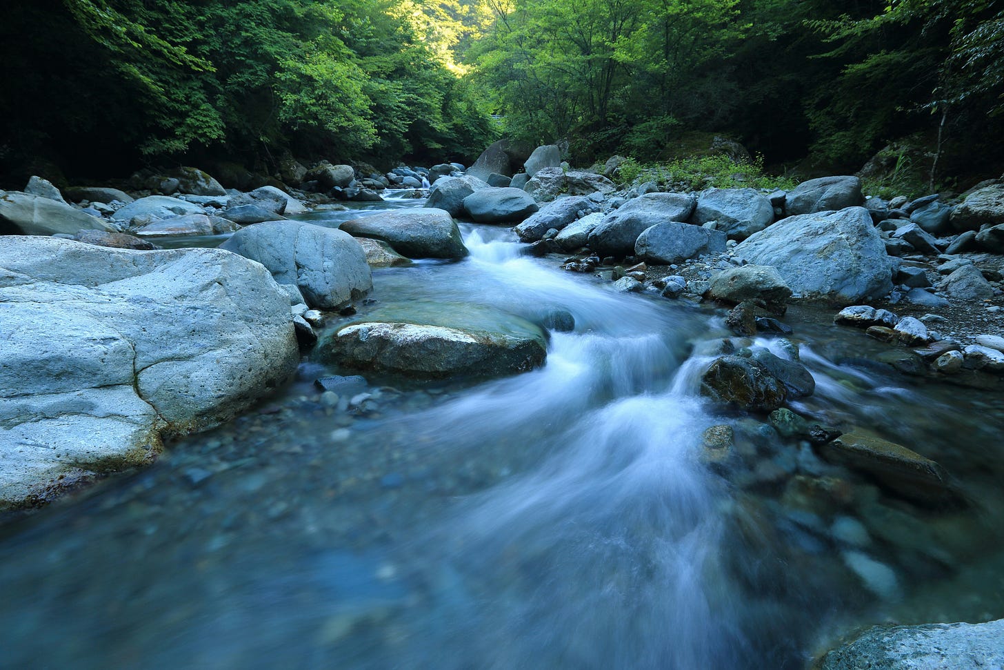 The flow of water over boulders in a river bed. Water is consistent in the path it’ll take, and yet appears to be free. [Credit: Kazuend on Unsplash]