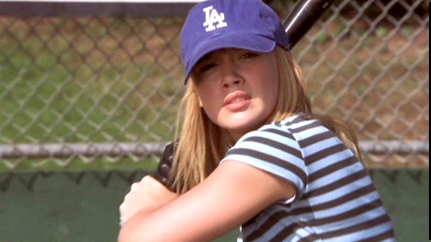 A still from A Cinderella Story that shows Sam (played by Hilary Duff) in her LA Dodgers hat wearing her blue-striped shirt, up to bat