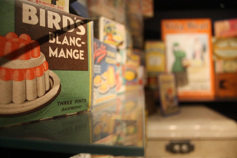 Food packaging in display case with Bird's Blancmange in foreground and other packets out of focus in background.