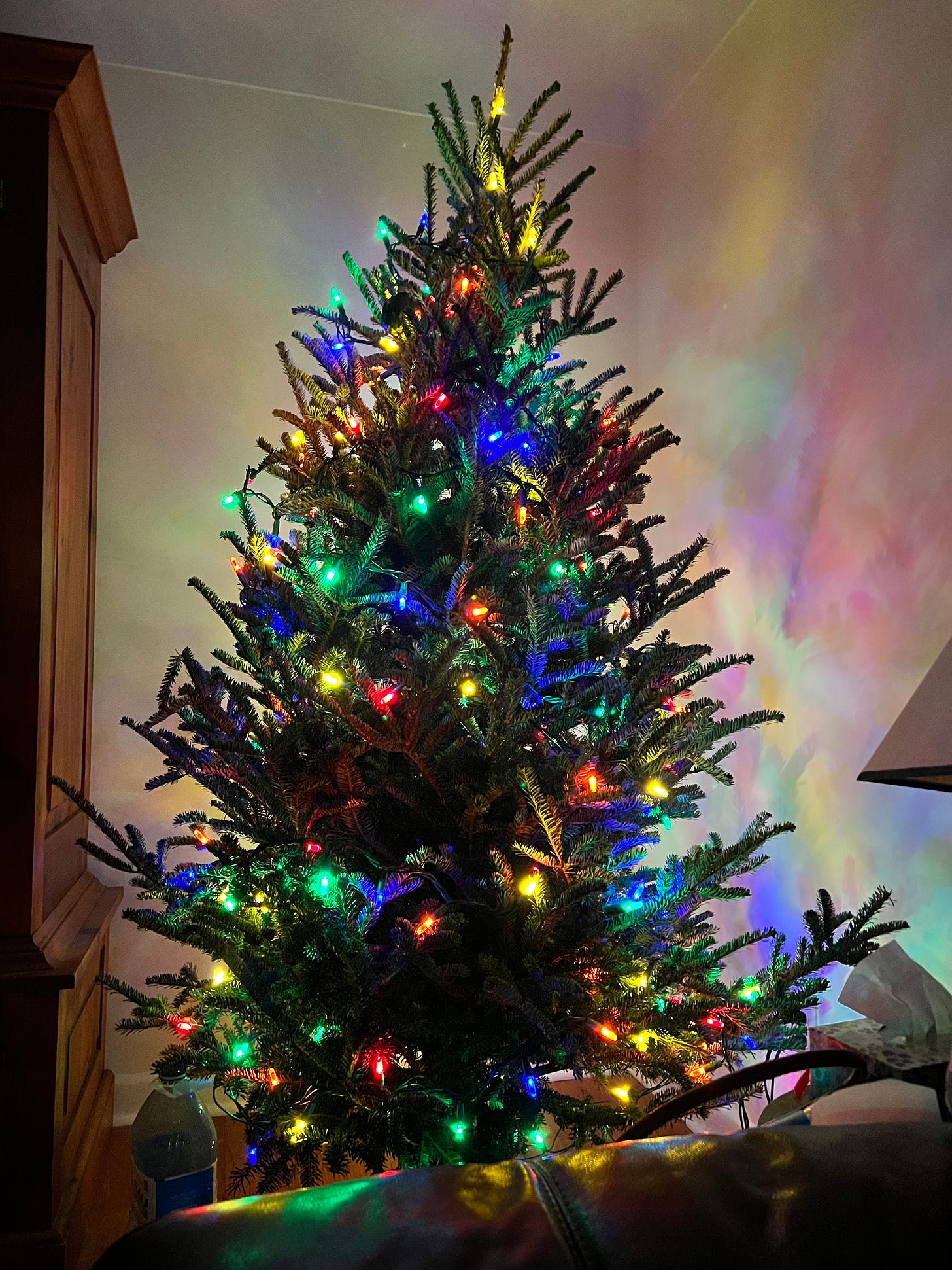 A christmas tree with coloured lights on in a darkened corner.