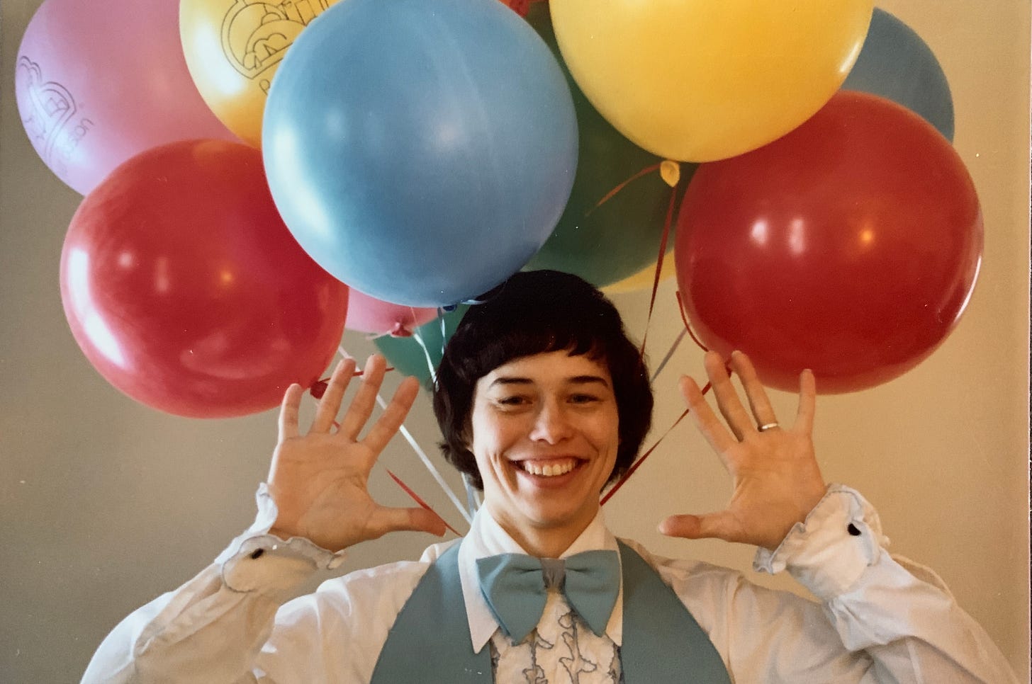 A woman in a bow tie and matching vest with a bouquet of balloons behind her head