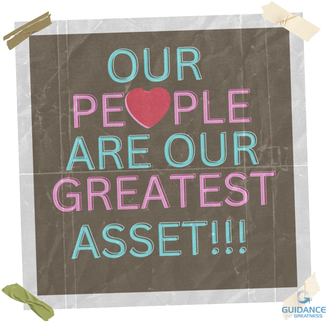 A poster reading “our people are our greatest asset!!!” In colorful letters on a dark background with a white border. The “o” in “people” was replaced with a red heart.  The poster is slightly crooked and has crumbled pieces of tape in each corner. The poster is wrinkled and dull.