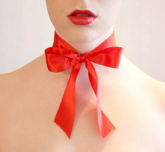 White woman headshot with red lips & red bow around neck