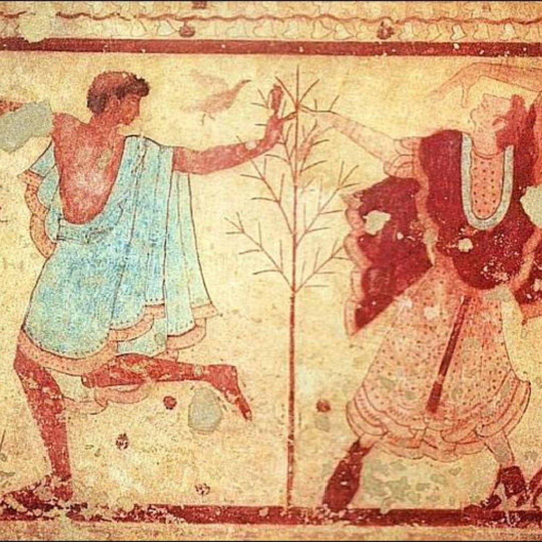 An ancient etruscan mosaic depicting two people dancing. The figure on the left is dark-skinned with tight curled hair and a blue robe. The figure on the right is light-skinned with red-brown hair and red and white robes. The two touch hands through what seems to be a small tree of just branches, no leaves. 