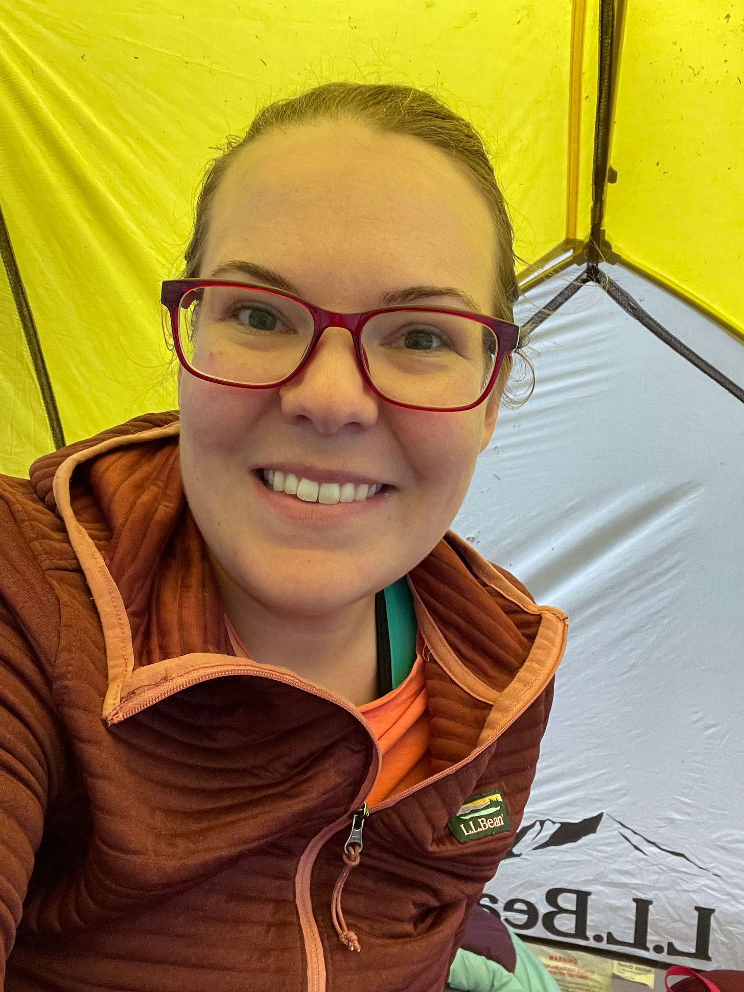 The author wearing red red glasses and a red hooded sweatshirt inside a yellow and grey tent.