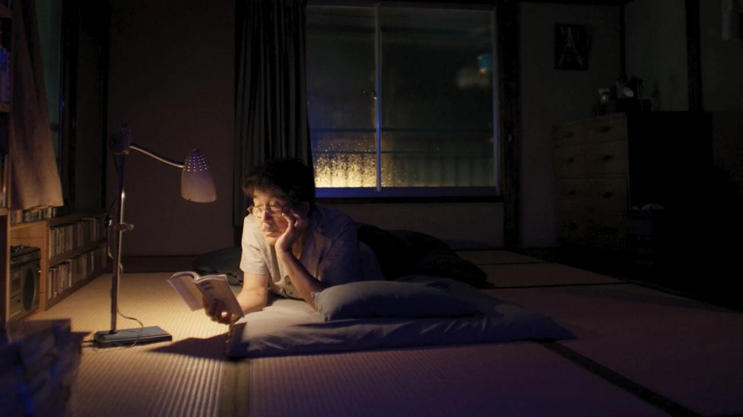 hirayama (from Perfect Days) lying down on his bedroom floor at night and reading a book