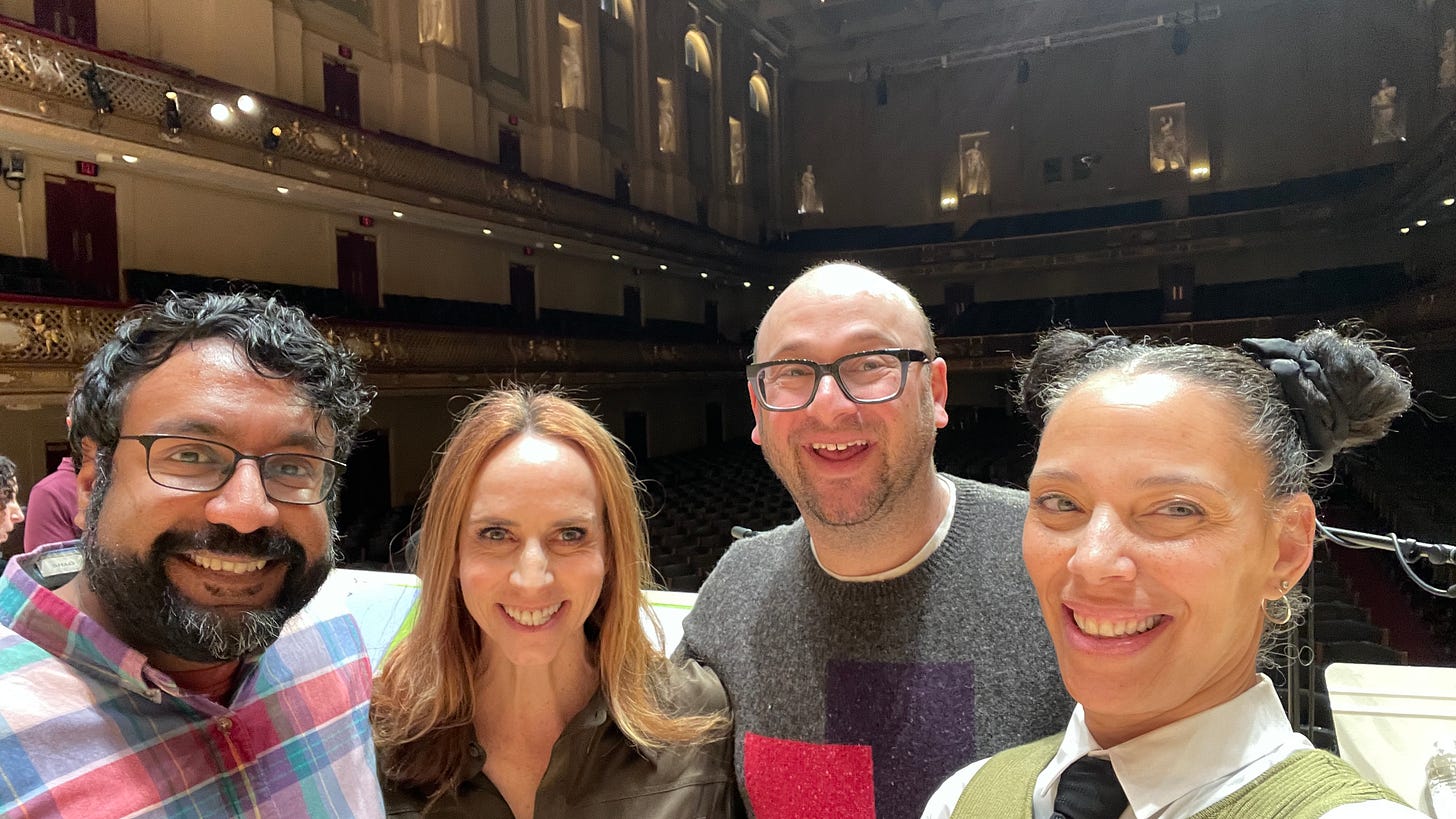 Hari, Faith, me, and Bethany on stage at Symphony Hall in Boston, with the seats and chandeliers in the background.