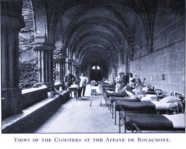 A black and white photograph showing a view of the cloisters at the Abbey of Royaumont during WW1 with a row of beds occupied by patients on the right.