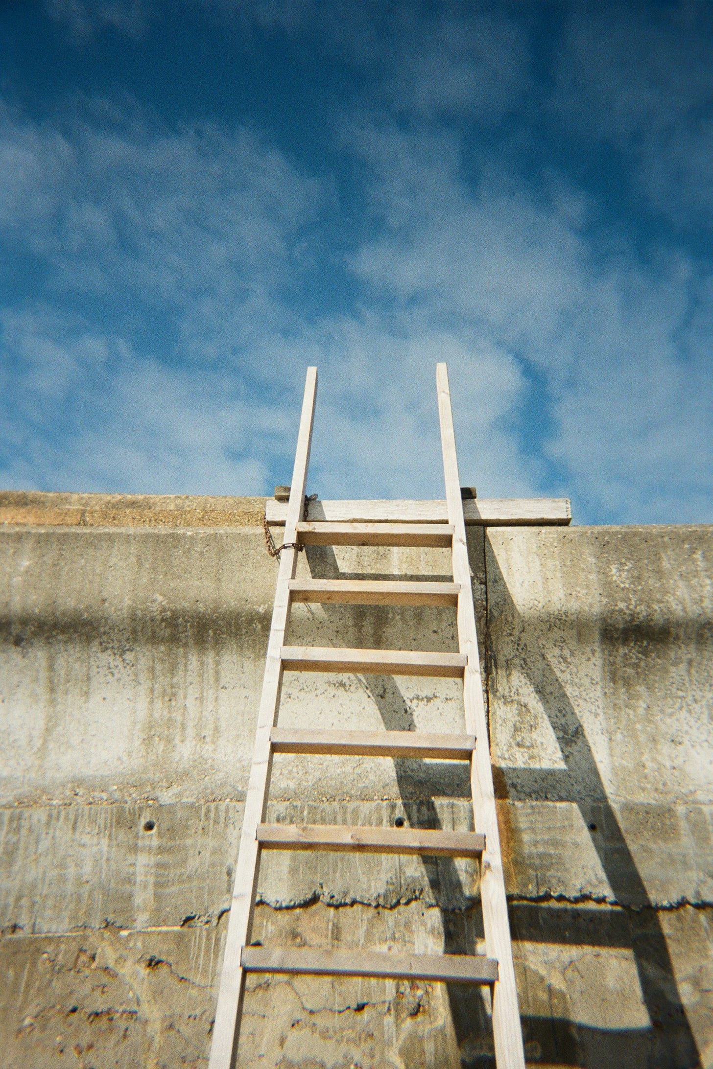 photo of a ladder in place to climb a wall and reach the blue sky beyond