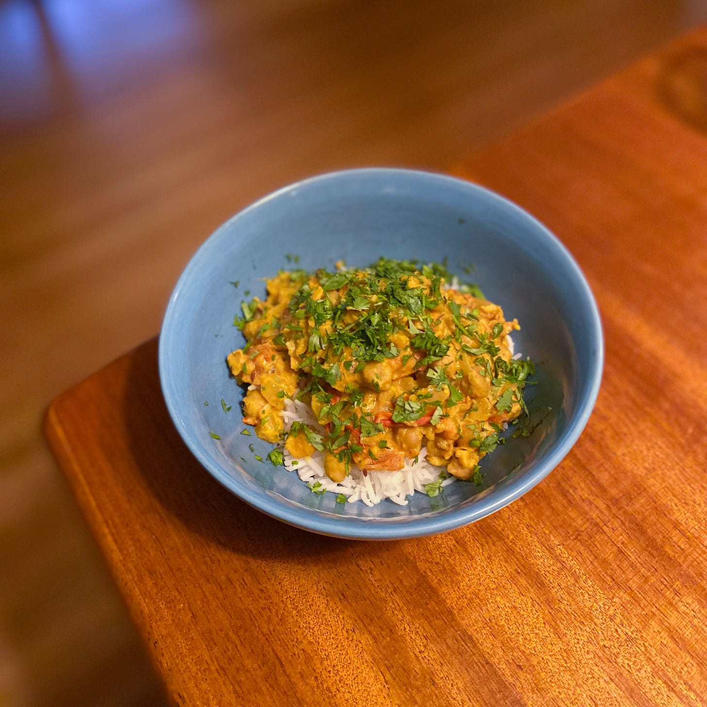 A blue bowl of chana masala over basmati rice with lots of cilantro on top.