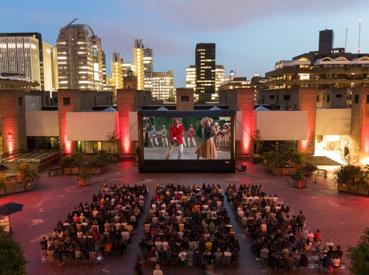 People sitting on chairs in rows outside at Barbican, watching a film on a large screen