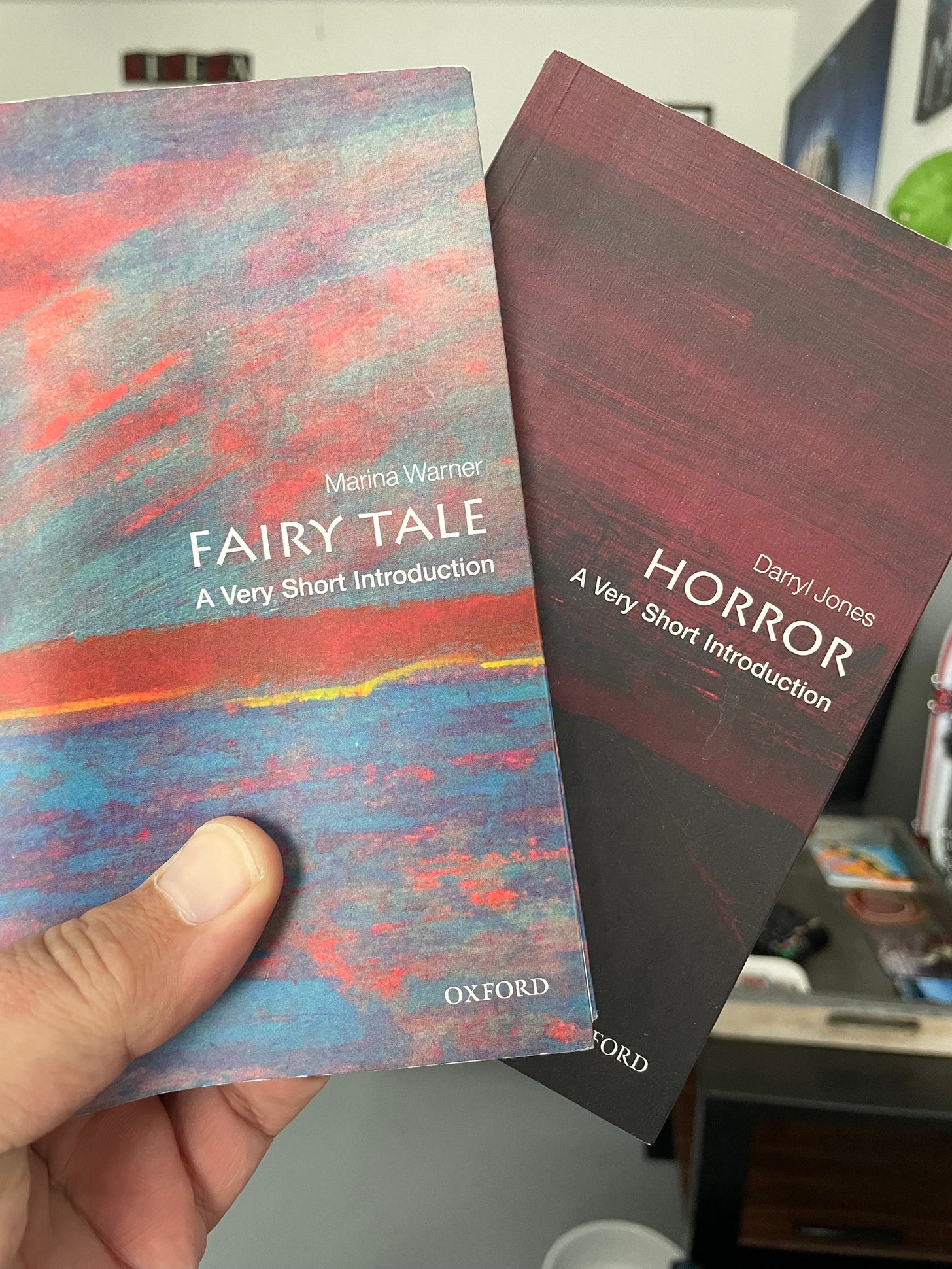 A hand holding two books (Horror, Fairy Tale) from A Very Short Introduction Series of books by Oxford Press