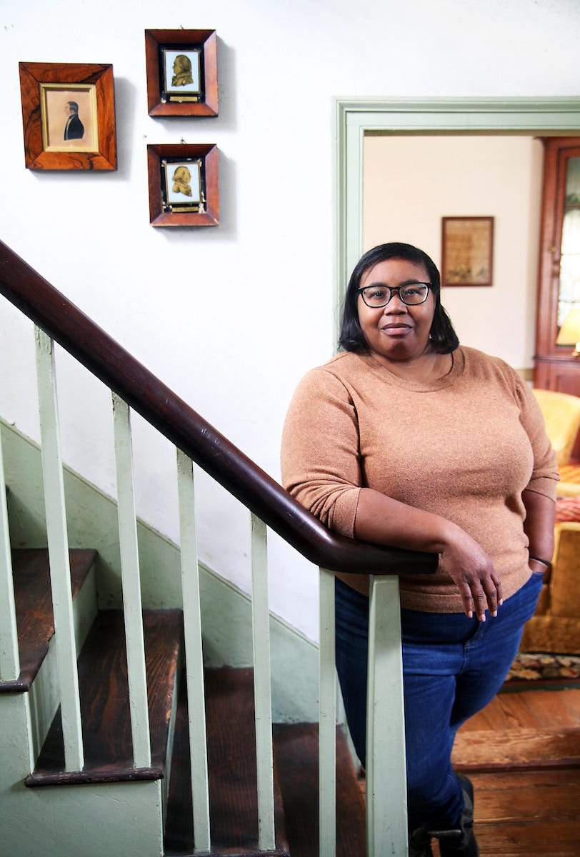 An African American woman stands at the bottom of a staircase looking directly at the camera