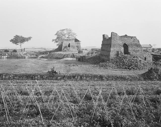 Image 1 black and white photograph that shows open Vietnamese countryside with two ancient stone buildings damaged by shelling and war. 