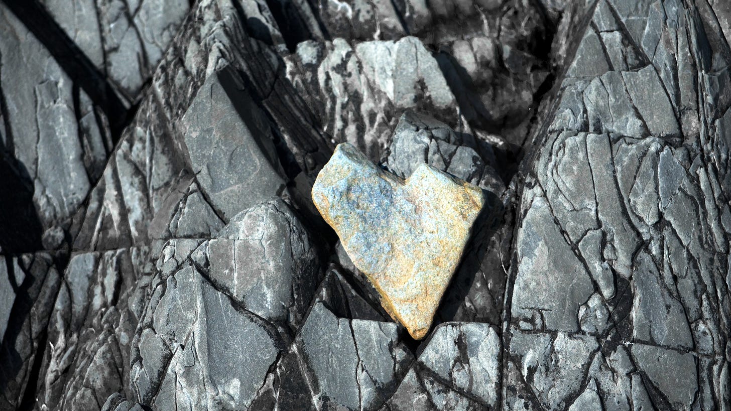 A heart-shaped stone rests in the cracked layers of a cliff face.