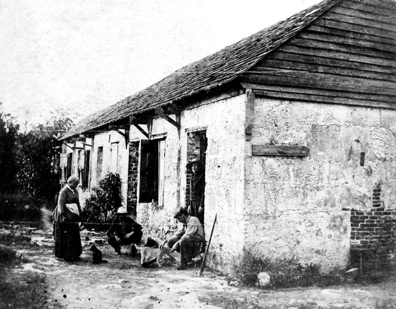 Colonel James W. Ewan (squatting), at entrance of the Fort Dallas Barracks building, aka slave plantation house, in the 1870s.