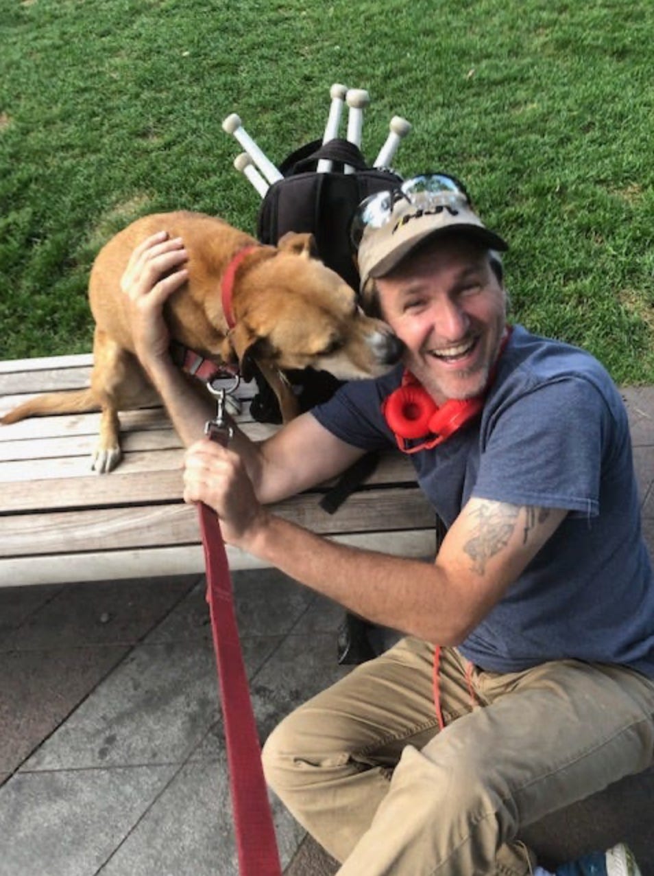 A dog nuzzles a man's face, a backpack with juggling sticks is behind them.