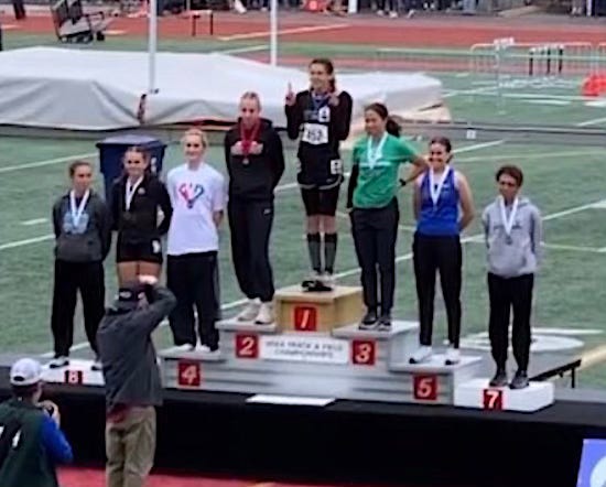 A tall, broad-shoulder boy stands on the top of the podium in the first place position