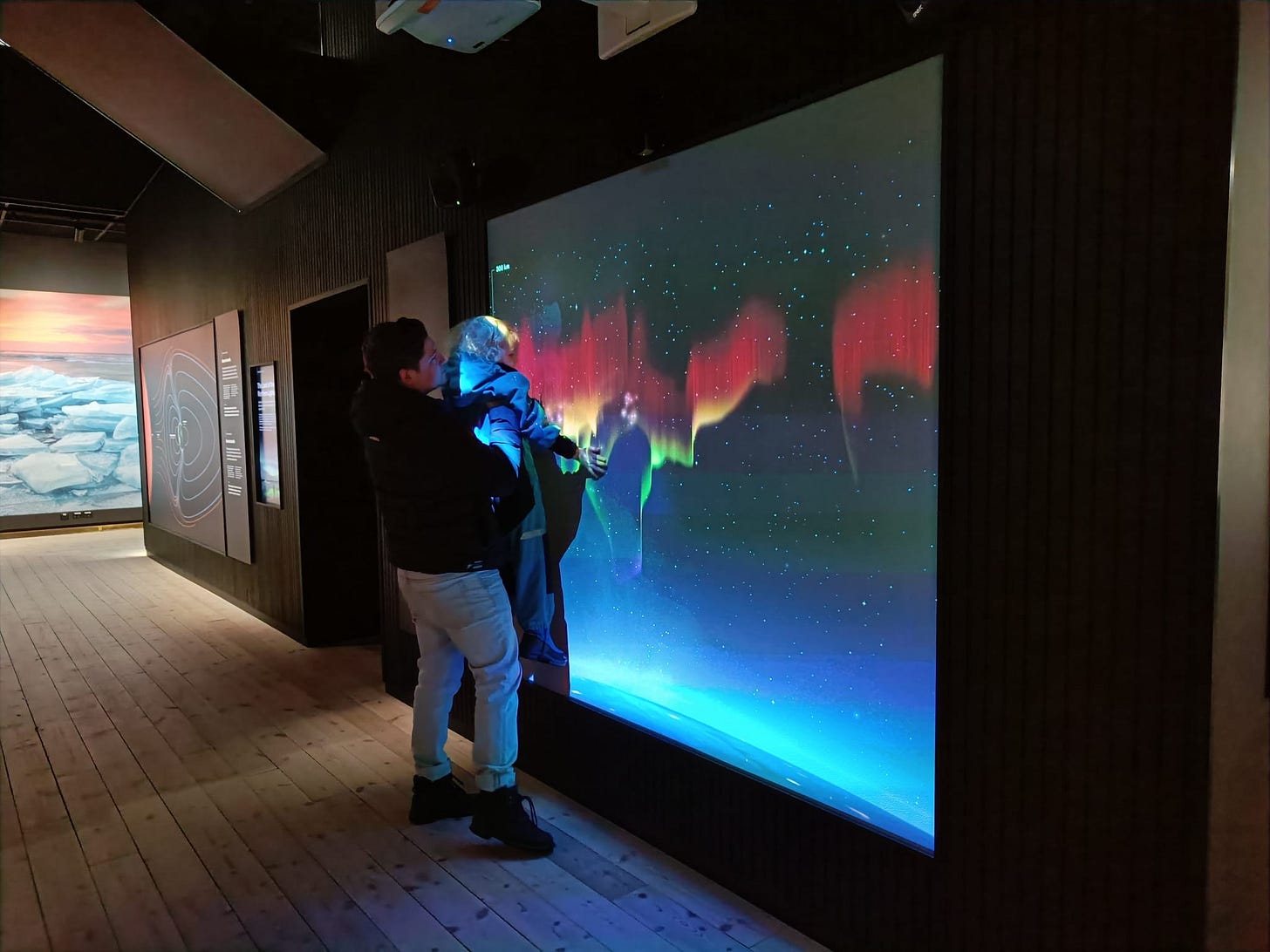 a man holds a child against a screen depicting the northern lights