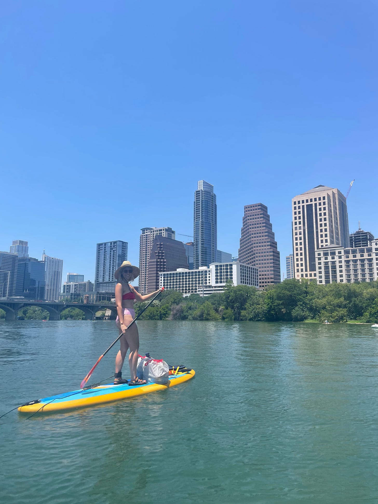 A woman paddleboards on Lady Bird Lake with downtown Austin behind her.