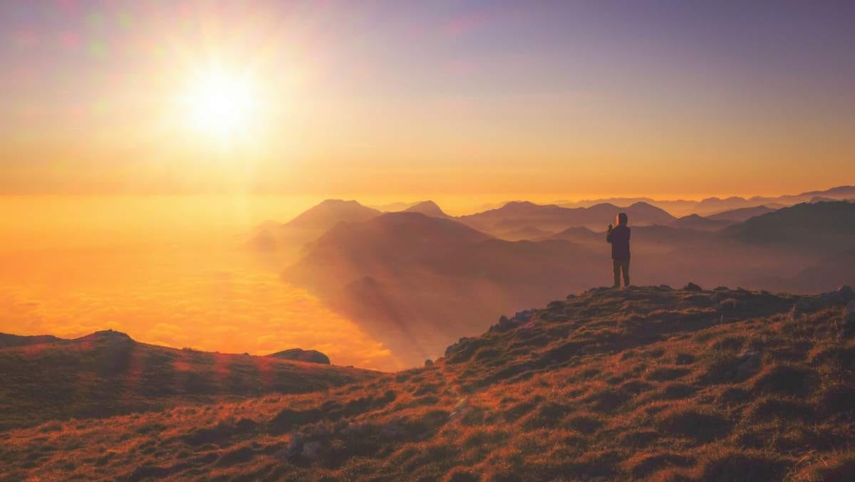 Photo taken at sunset of figure overlooking a sunlit golden landscape half-covered in cloud.