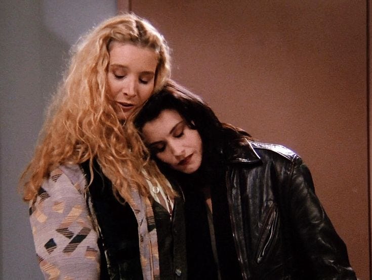 This may contain: two women standing next to each other looking at a cell phone