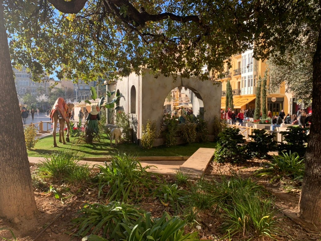 A life-size Nativity scene is framed by trees and plants.