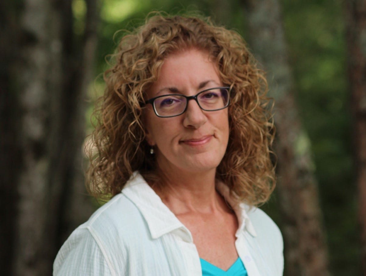 Paulla Estes Book Coach photographed in the summer forest smiles directly at camera 