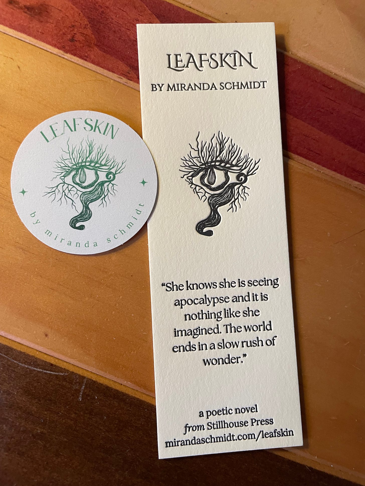 a bookmark and sticker with the title Leafskin, featuring the eyetree image from the book cover