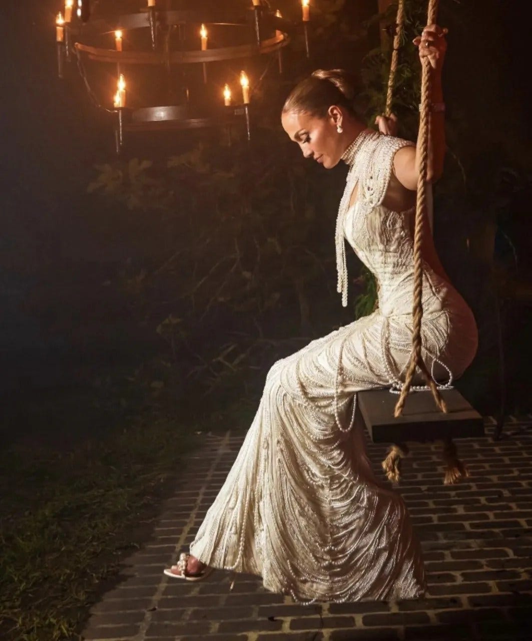 Jennifer Lopez in her pearl-adorned wedding dress, sitting on a wooden swing.