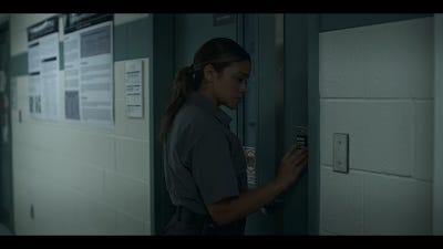 Screenshot from Awake 2021, showing hallway with posters on right of Gina Rodriguez opening a door.