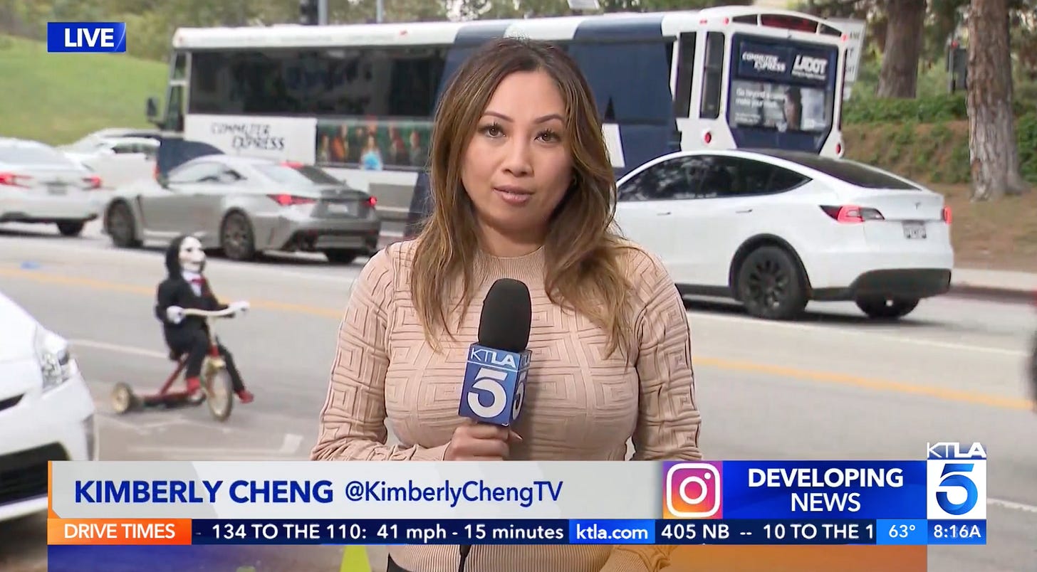 Screenshot from a live hit by KTLA TV’s Kimberly Cheng where Billy pedals his tricycle past in the near background just as Cheng signs off.