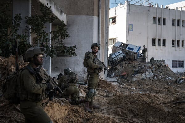 Soldiers standing on bare earth outside a concrete building, with overturned U.N. vehicles in the distance.