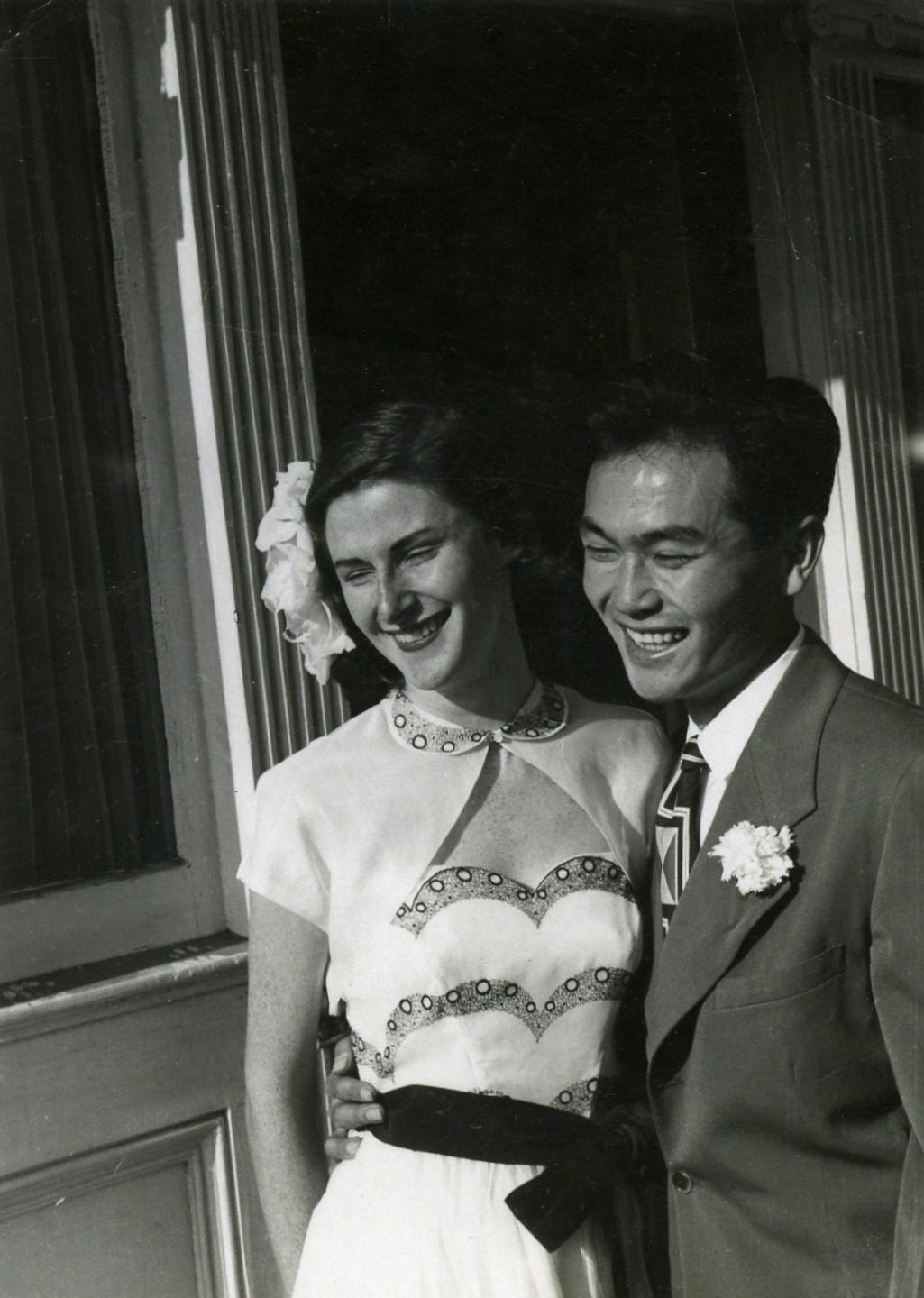 A black and white photo of Dorothy Walker and Joe Kamiya with their arms around each other and smiling in front of a house
