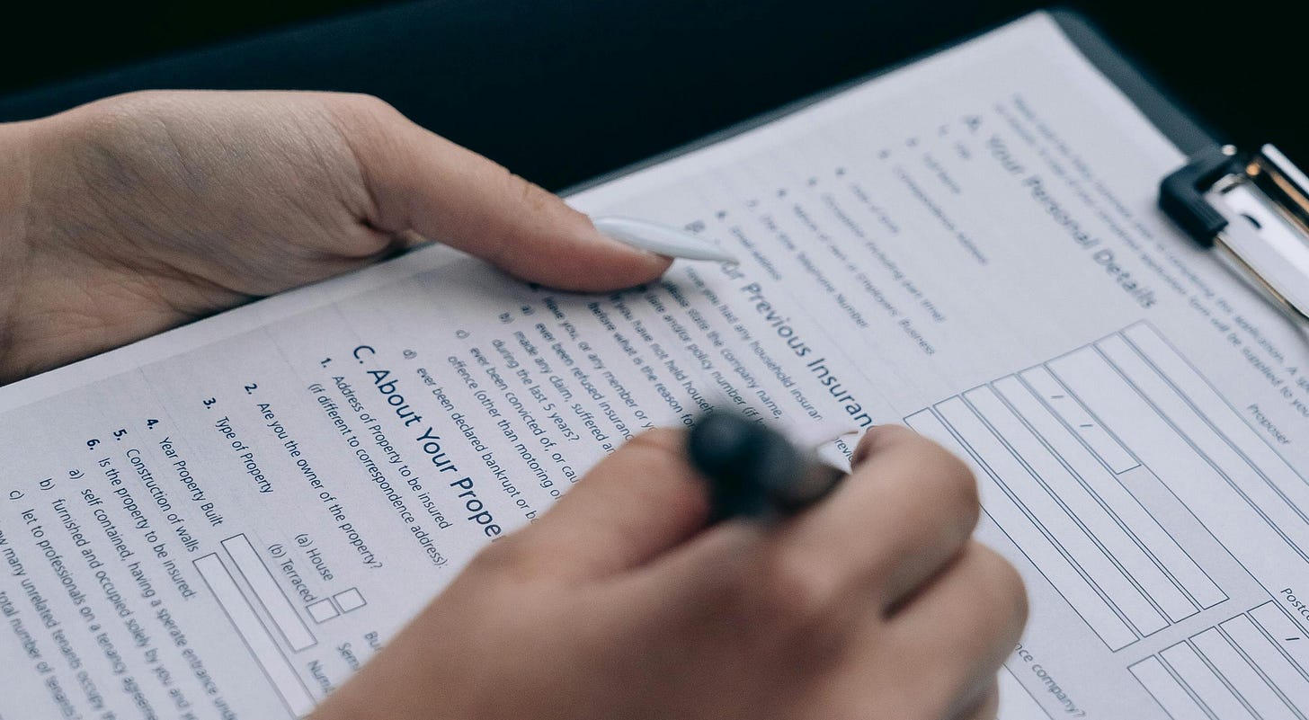 An image of a woman with long white nails filling out paperwork on a clipboard.