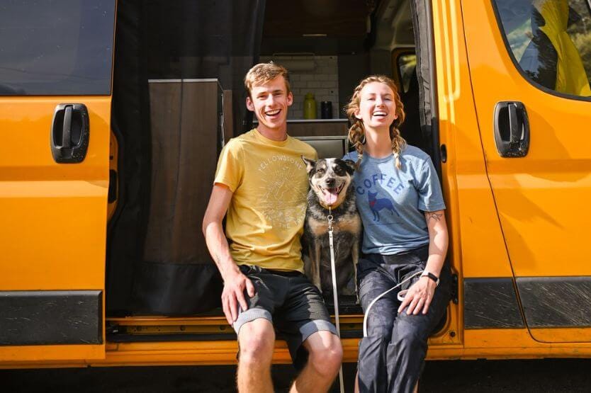 Sean, Scout the blue heeler, and Haley sit on the sliding door step of our bright yellow converted RAM promaster van