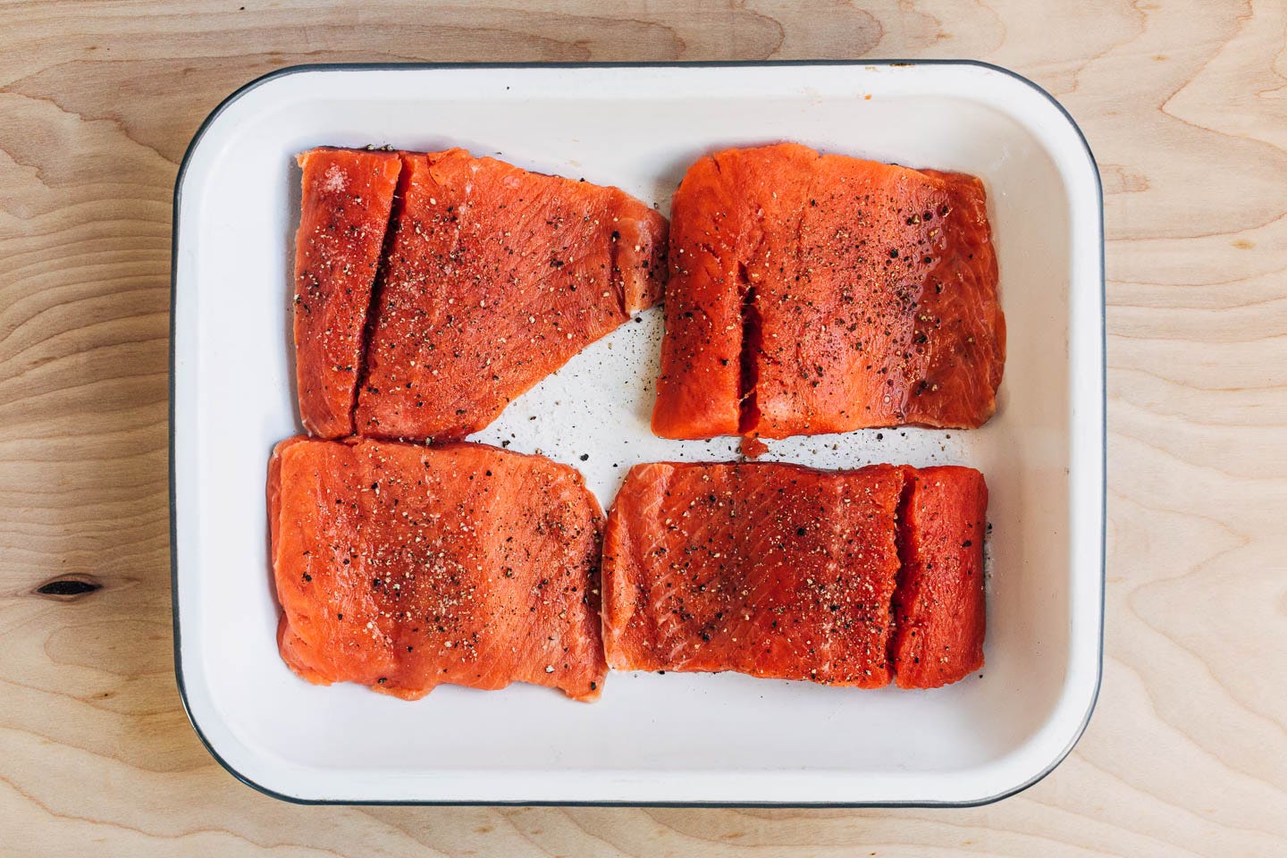Raw salmon filets in a dish with salt and pepper on top