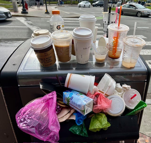 A group of plastic cups and a trash can on a street corner

Description automatically generated