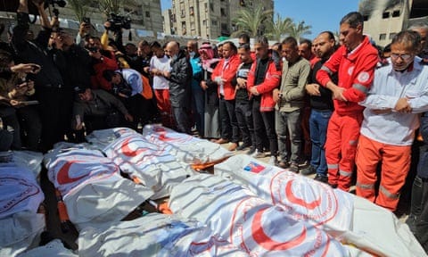 People stand around bodies wrapped in shrouds