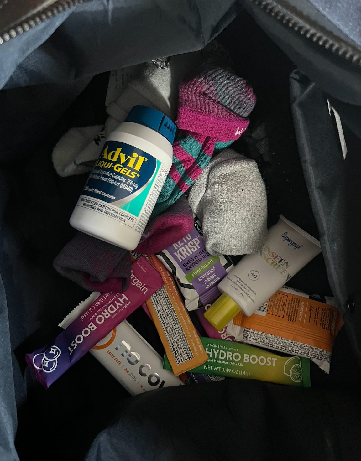  The inside of Amber's duffle bag. It has a bottle of Advil, a few pairs of socks, sunscreen, hydration powder sticks, and snack bars.
