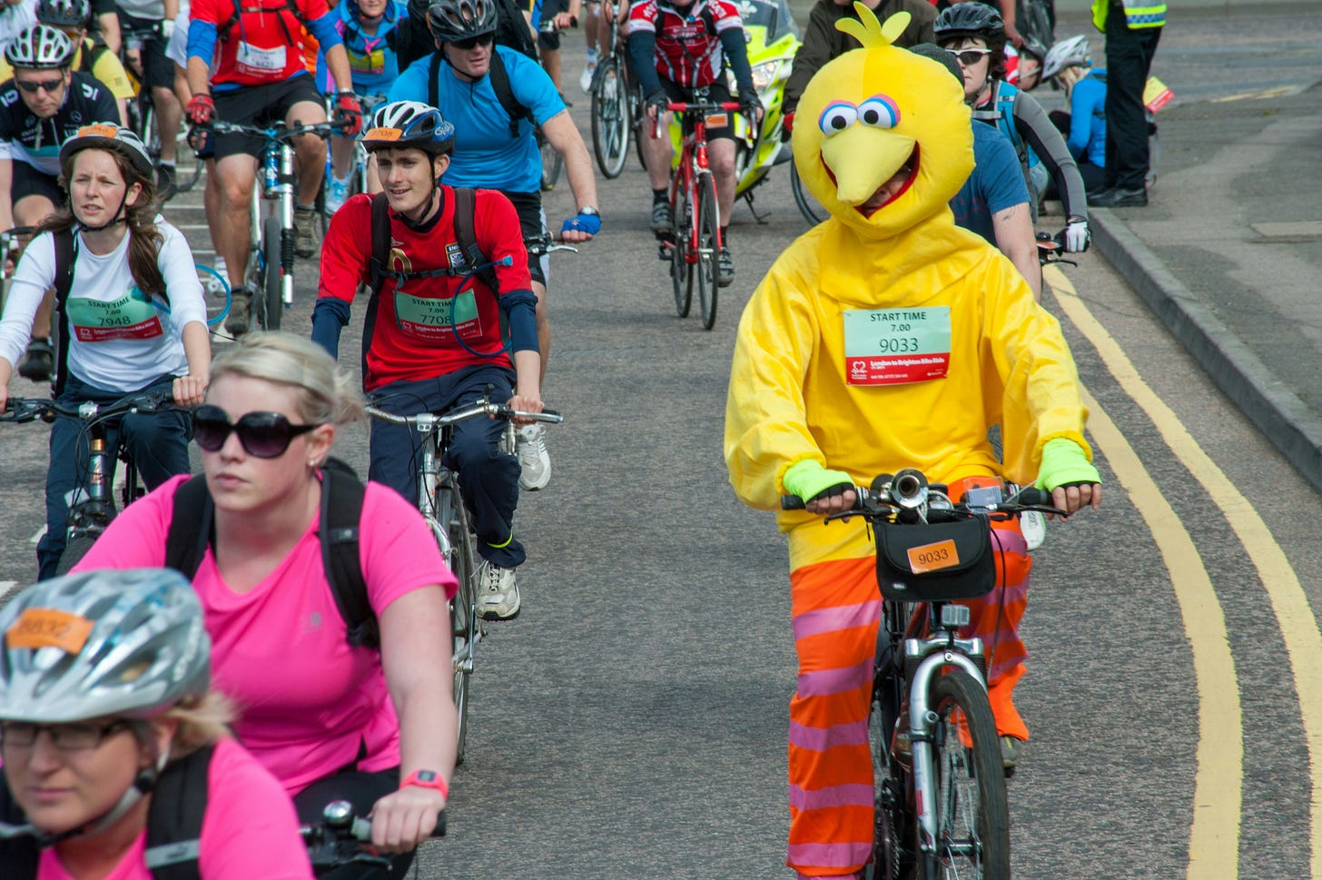 front facing image of a charity cycle ride where participants dress normally with the exception of one dressed in a yellow big bird costume